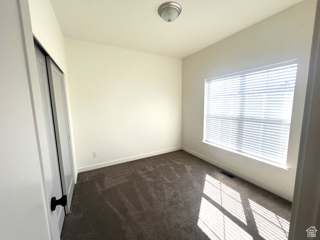 Unfurnished bedroom with a closet, baseboards, visible vents, and dark colored carpet