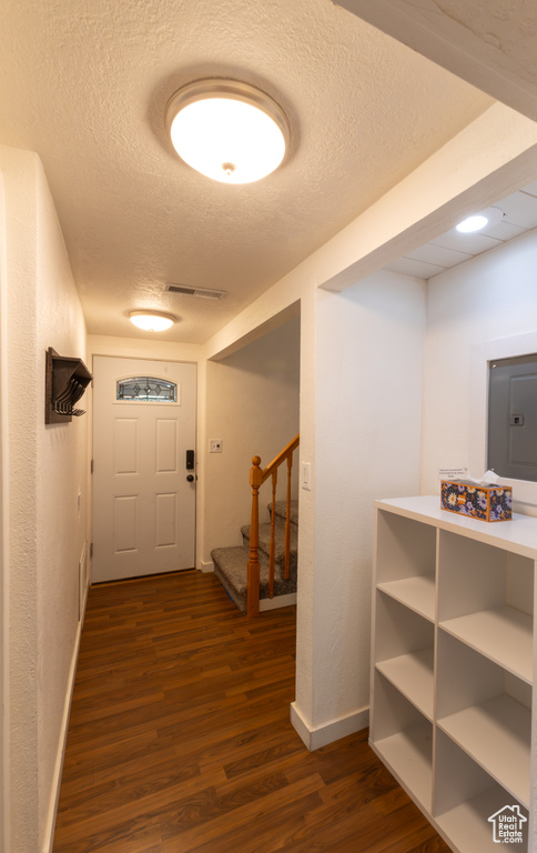 Corridor featuring a textured ceiling, visible vents, dark wood finished floors, stairway, and baseboards