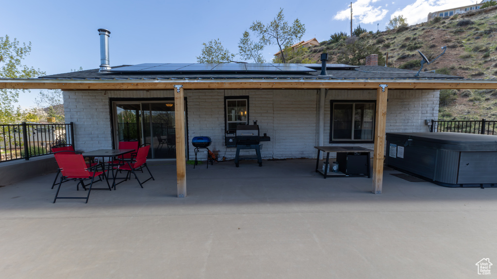 Back of property with solar panels, a hot tub, and a patio area