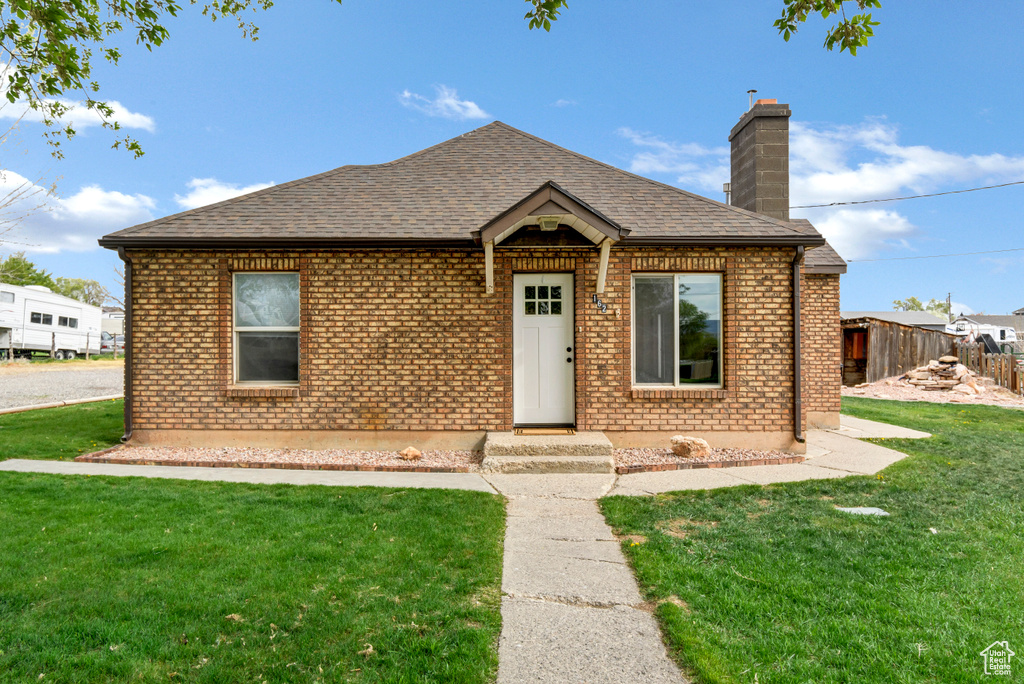 Bungalow featuring fence, a shingled roof, brick siding, a front yard, and a chimney