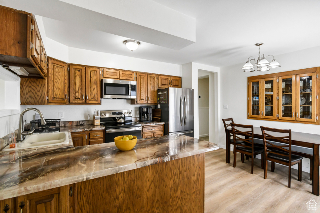 Kitchen with brown cabinets, a sink, a peninsula, an inviting chandelier, and stainless steel appliances