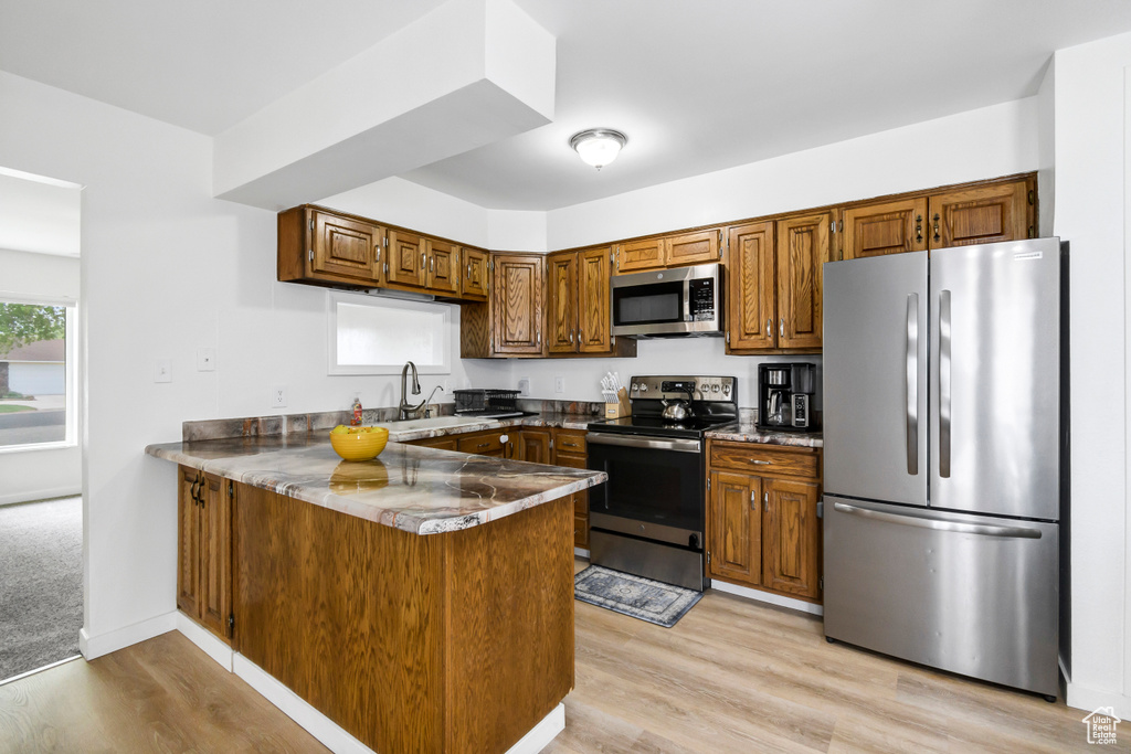 Kitchen with brown cabinetry, a peninsula, a sink, light wood-style flooring, and stainless steel appliances