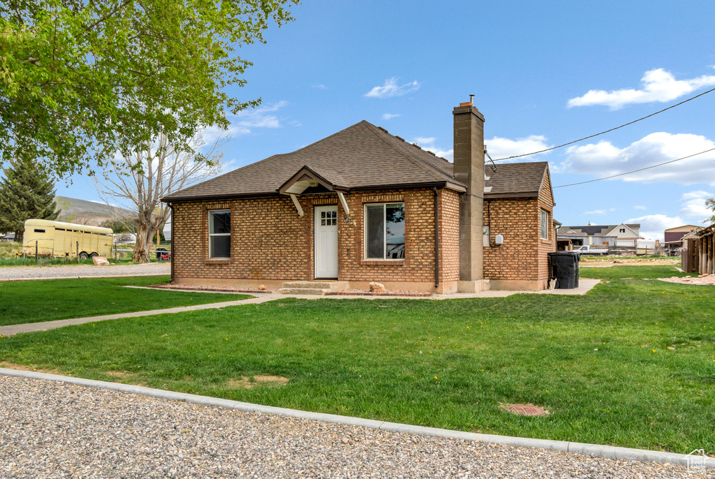 Single story home featuring roof with shingles, a chimney, a front yard, and brick siding