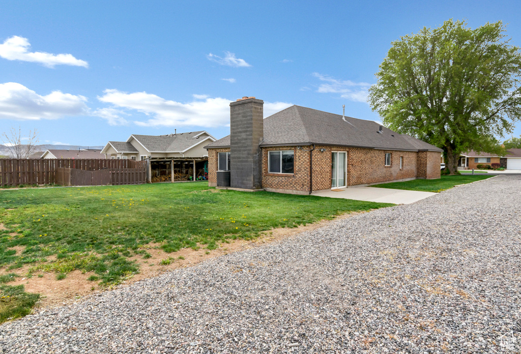 Back of house featuring a chimney, roof with shingles, a lawn, brick siding, and fence
