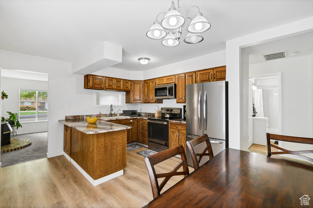 Kitchen featuring appliances with stainless steel finishes, light wood finished floors, brown cabinetry, a peninsula, and visible vents