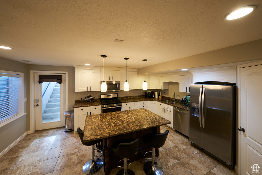 Kitchen featuring a kitchen island, a kitchen bar, a sink, stainless steel appliances, and white cabinetry