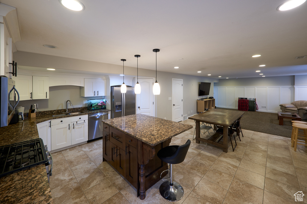 Kitchen with open floor plan, white cabinetry, a sink, dark stone countertops, and appliances with stainless steel finishes