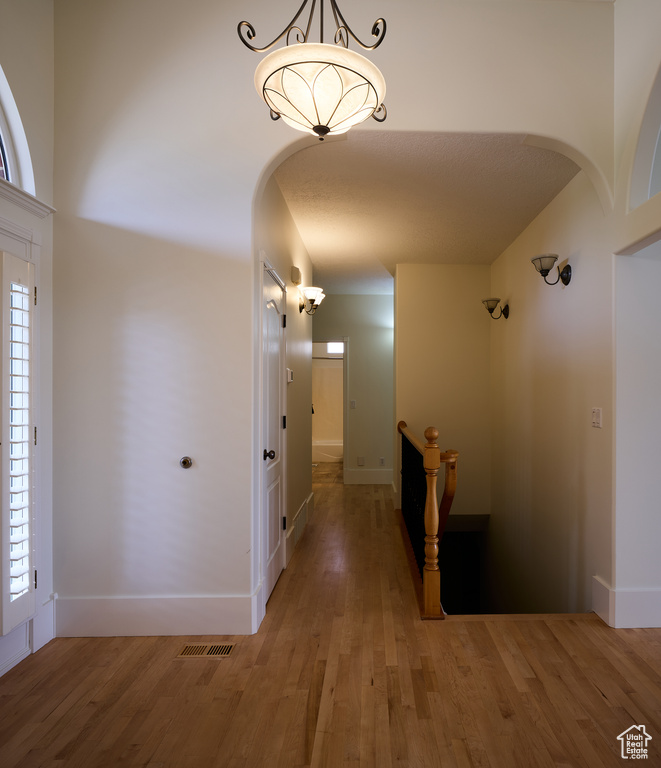 Hall featuring arched walkways, a healthy amount of sunlight, and light wood-style flooring