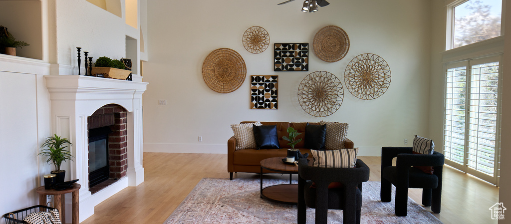Living area with light wood finished floors, a brick fireplace, a high ceiling, and a healthy amount of sunlight