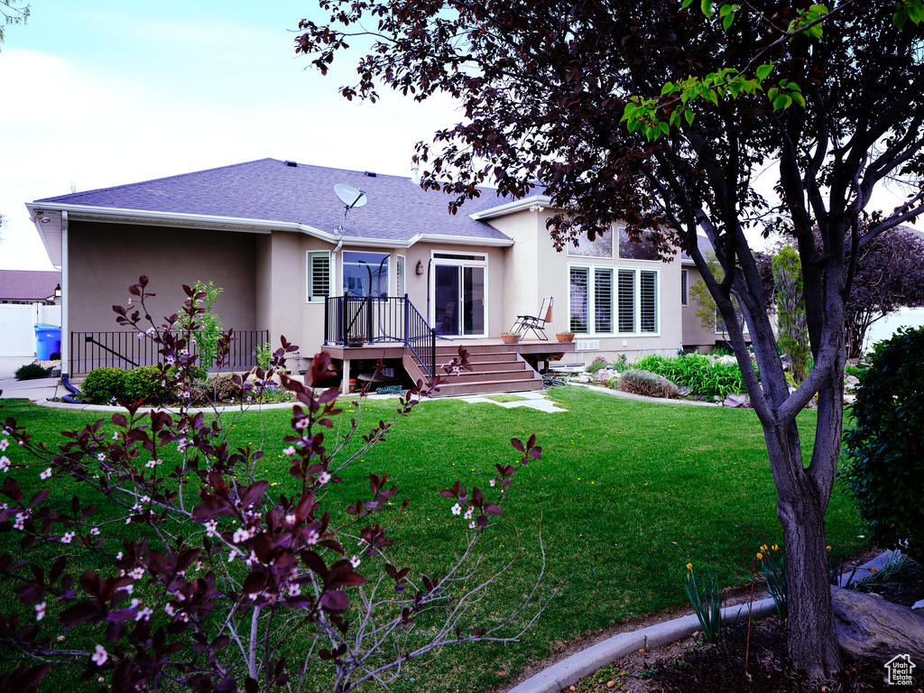 Rear view of property featuring a lawn, roof with shingles, and stucco siding