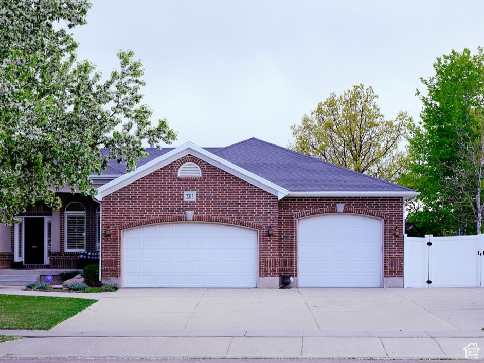 Ranch-style home with an attached garage, a front lawn, brick siding, a gate, and concrete driveway