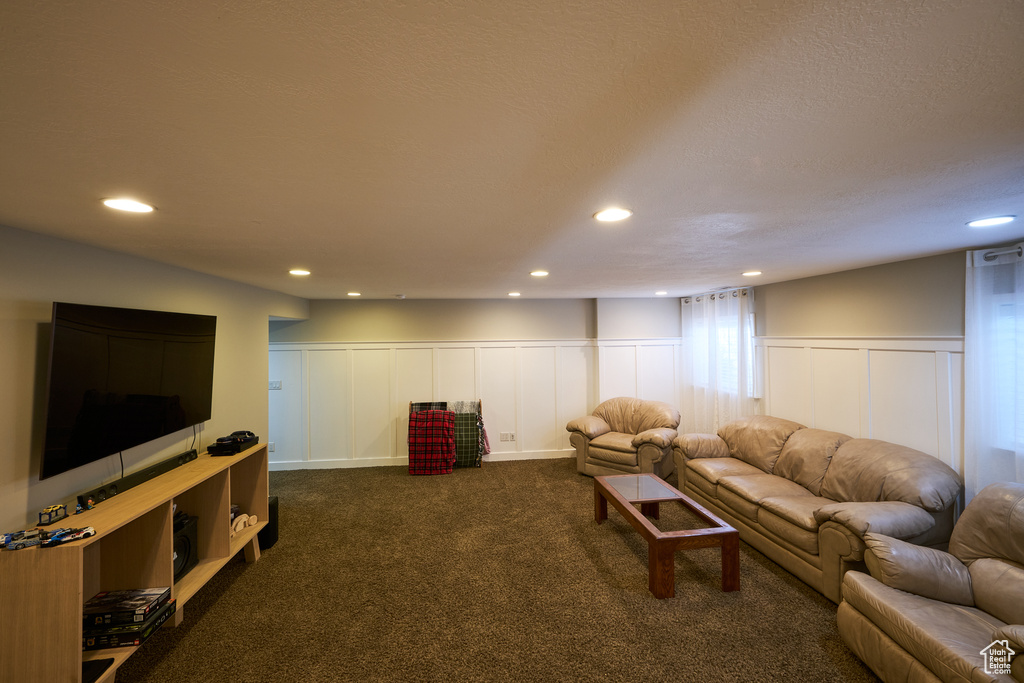 Living room featuring dark colored carpet, recessed lighting, wainscoting, and a decorative wall