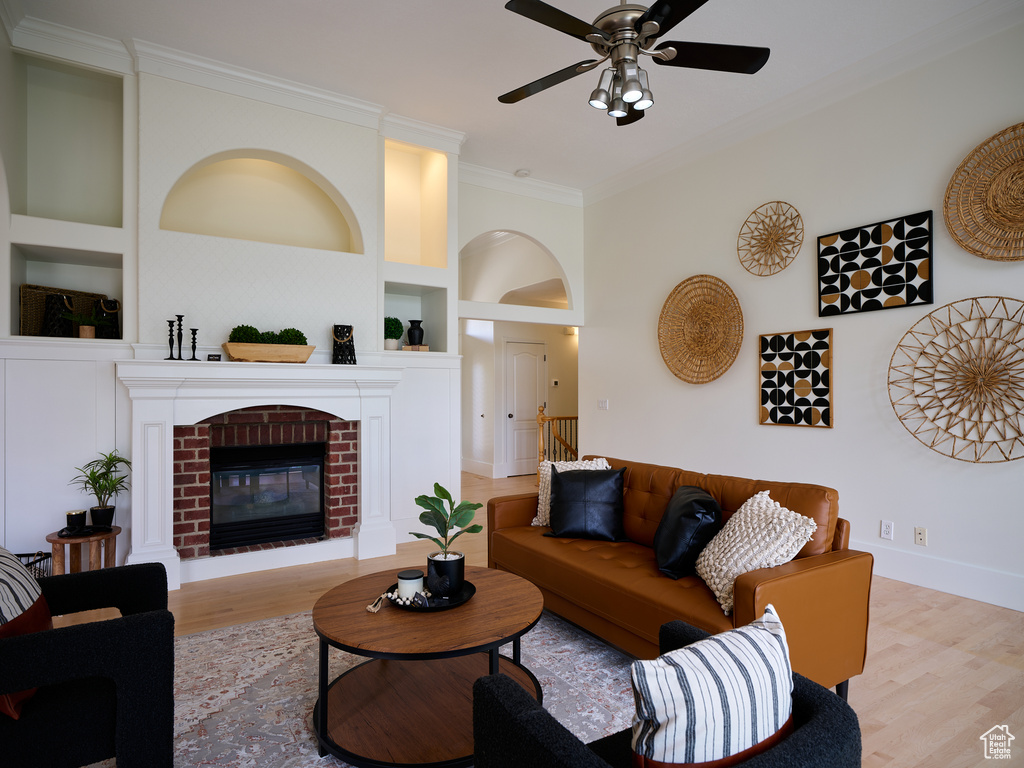 Living room with crown molding, built in features, a brick fireplace, wood finished floors, and a ceiling fan