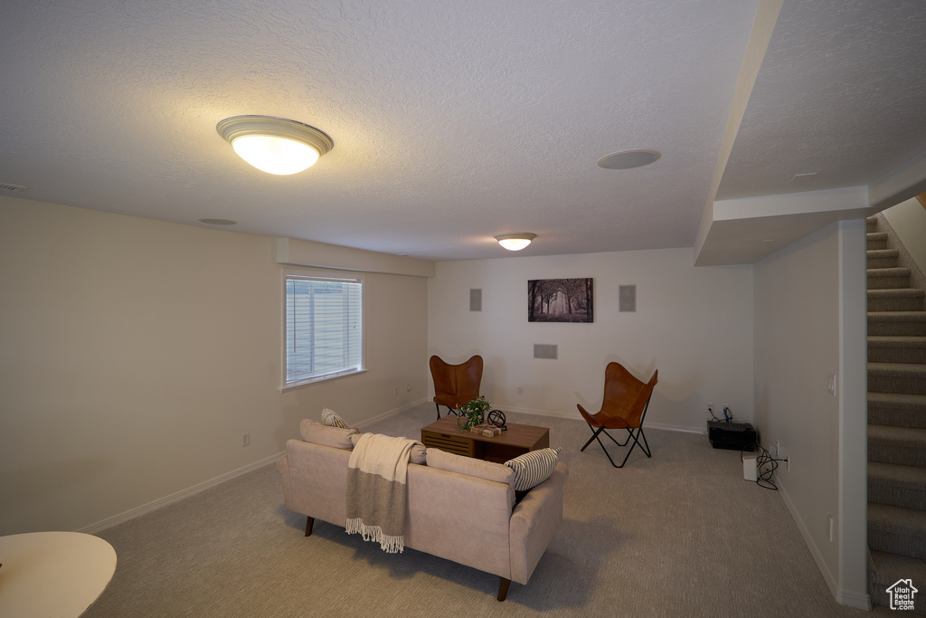 Living room featuring a textured ceiling, carpet, baseboards, and stairway