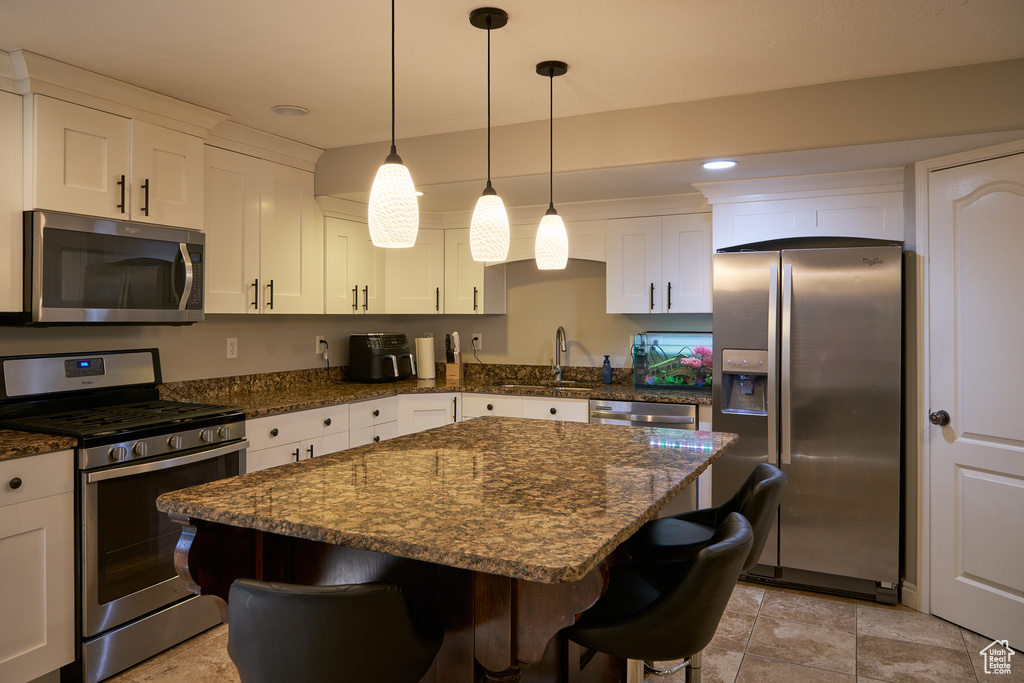 Kitchen featuring a kitchen island, a kitchen bar, white cabinets, a sink, and appliances with stainless steel finishes