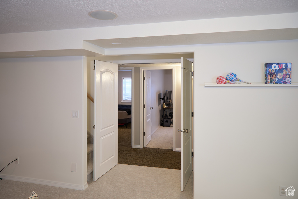 Hallway with baseboards, a textured ceiling, and light colored carpet