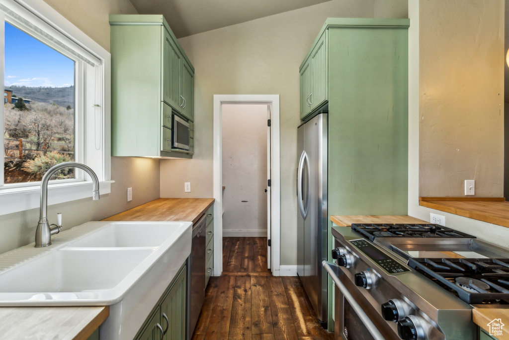 Kitchen with green cabinetry, a sink, stainless steel appliances, dark wood-type flooring, and light countertops