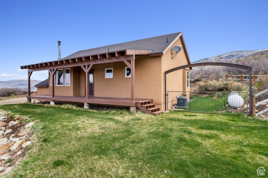 Rear view of property with fence, cooling unit, stucco siding, a shingled roof, and a lawn