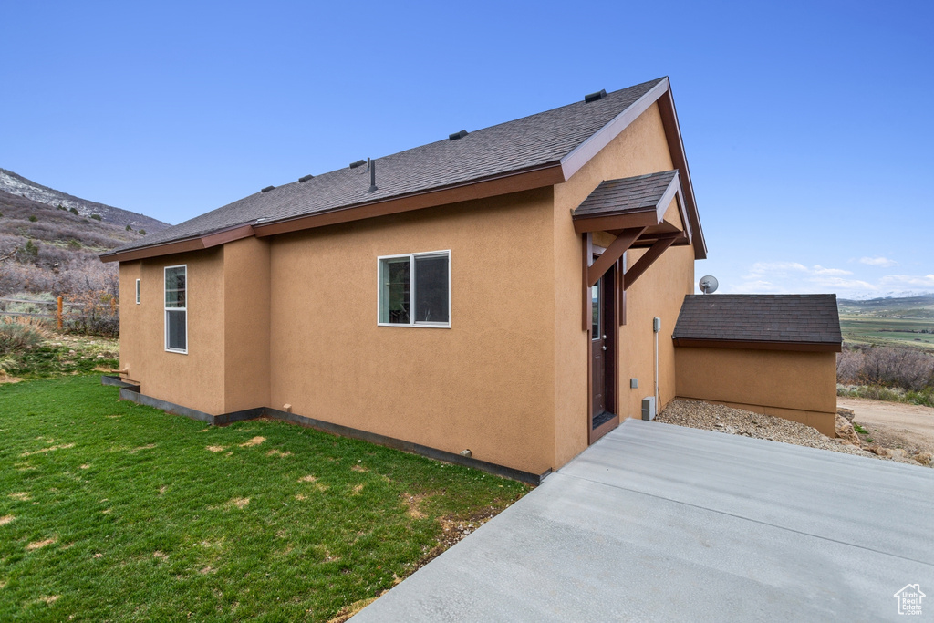 View of property exterior with a yard, stucco siding, a patio area, a mountain view, and a shingled roof
