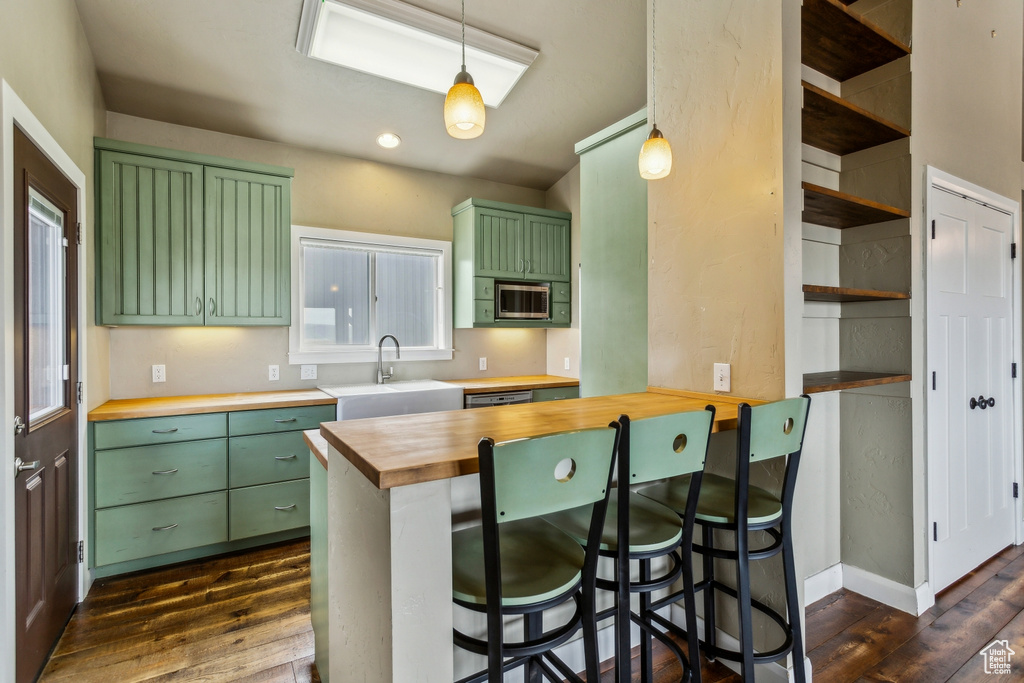 Kitchen with dark wood-style flooring, a sink, wood counters, stainless steel microwave, and green cabinets