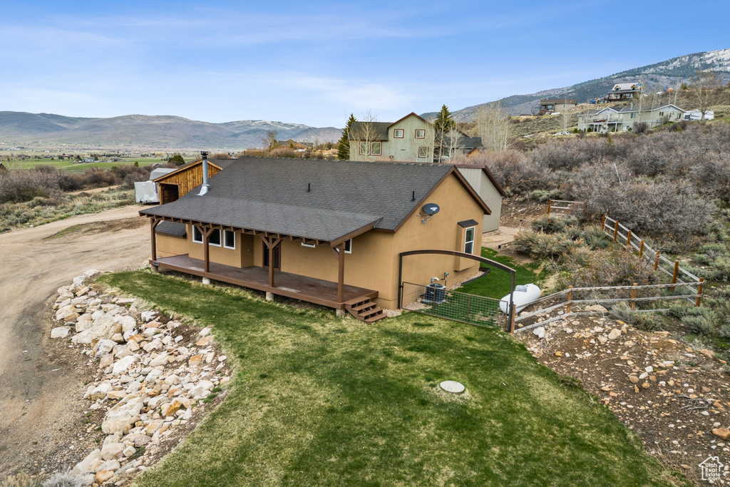 Rear view of house featuring fence, a mountain view, a yard, a shingled roof, and stucco siding