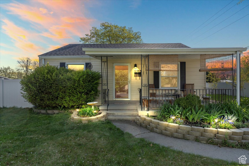 View of front of property featuring fence, a lawn, a porch, and a shingled roof
