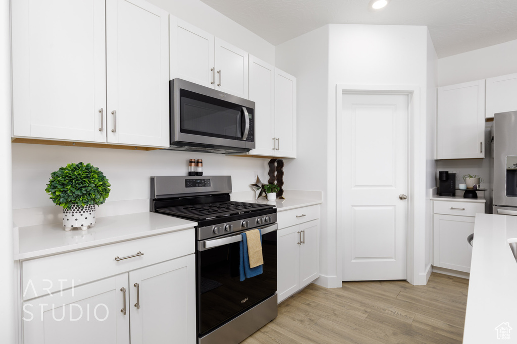 Kitchen with light wood finished floors, white cabinetry, stainless steel appliances, and light countertops