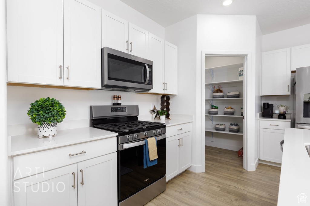 Kitchen featuring light wood-style floors, stainless steel appliances, light countertops, and white cabinets