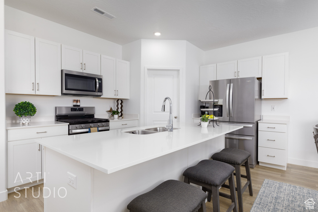 Kitchen featuring a breakfast bar area, a sink, visible vents, stainless steel appliances, and light wood-type flooring