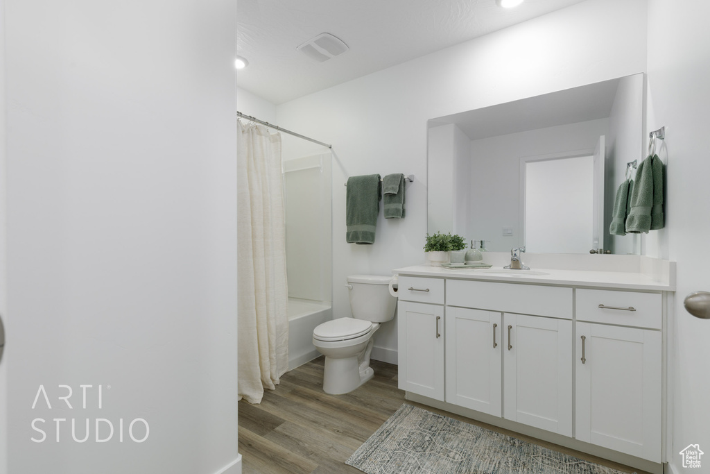 Bathroom with shower / bathtub combination with curtain, vanity, toilet, visible vents, and wood finished floors