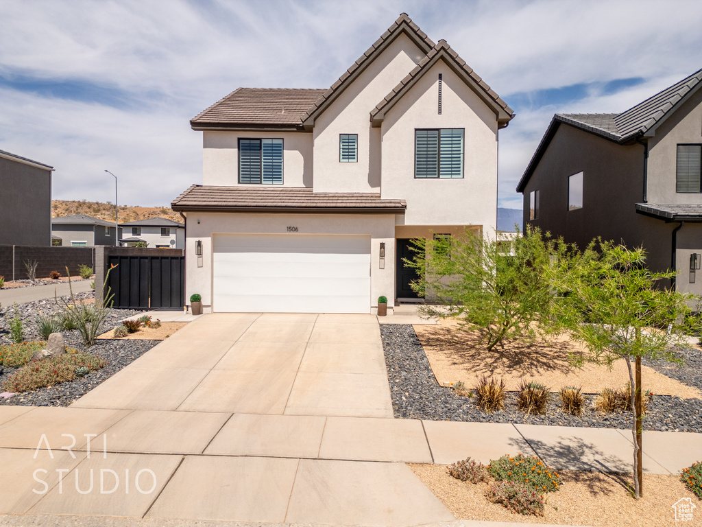 View of front facade with fence, concrete driveway, a tiled roof, stucco siding, and a garage