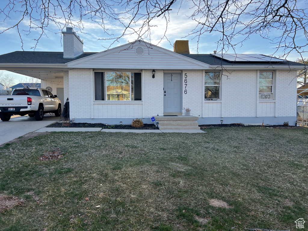 View of front of house with brick siding, a chimney, a front yard, and an attached carport
