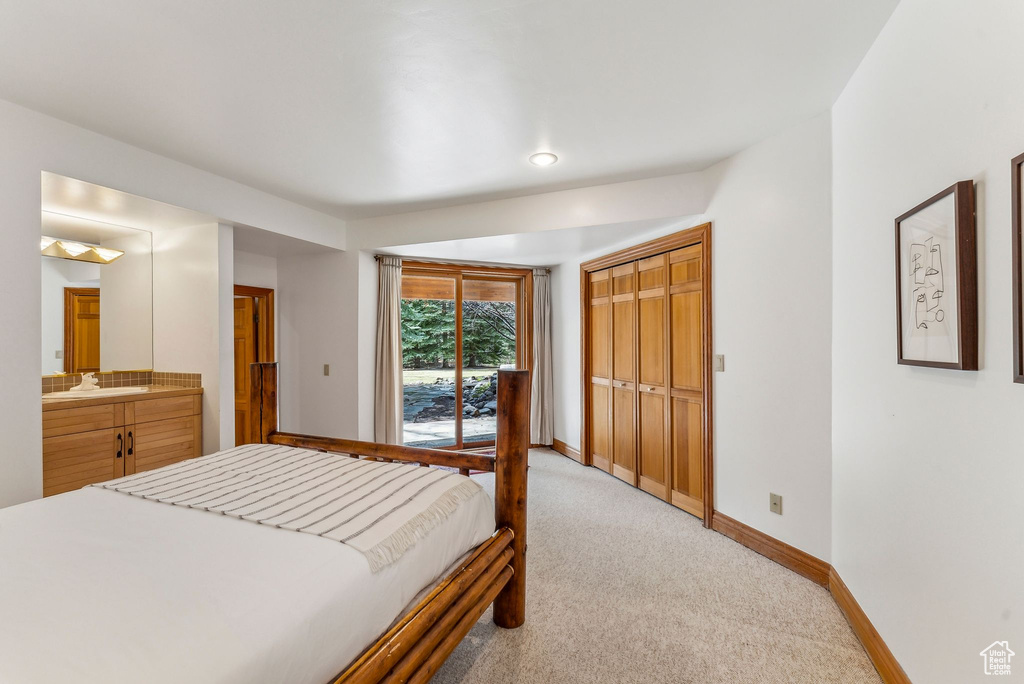 Bedroom with light colored carpet, access to outside, ensuite bathroom, a sink, and baseboards