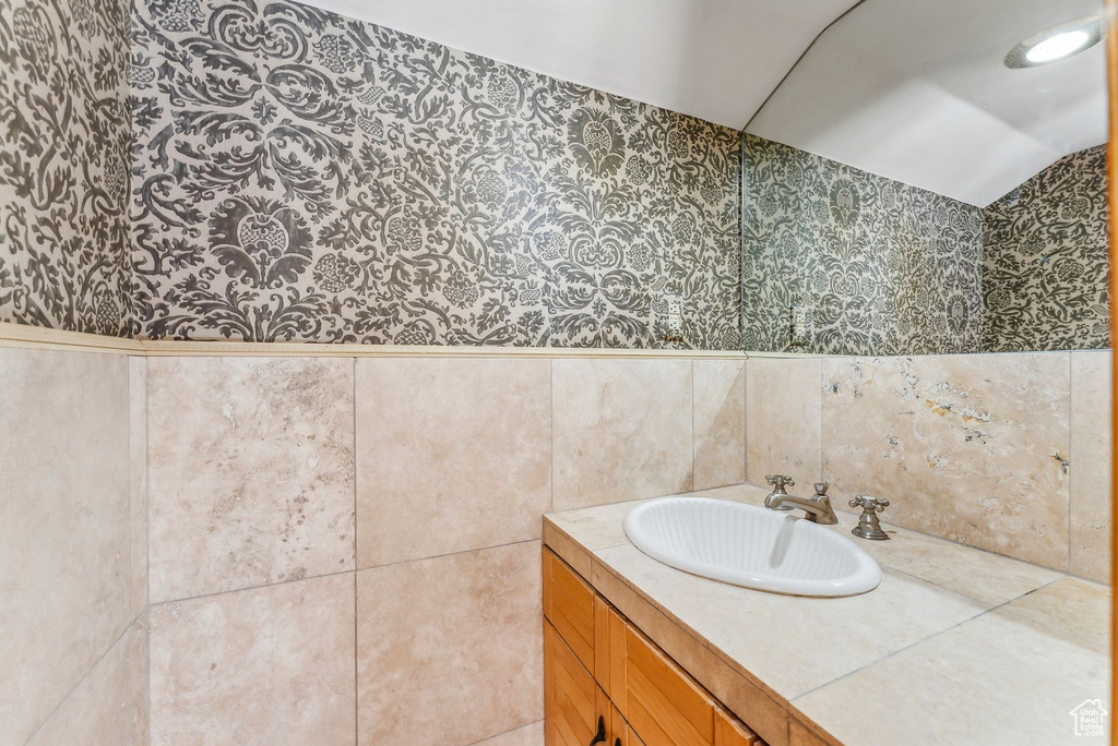 Bathroom with tile walls, wallpapered walls, vaulted ceiling, and a sink