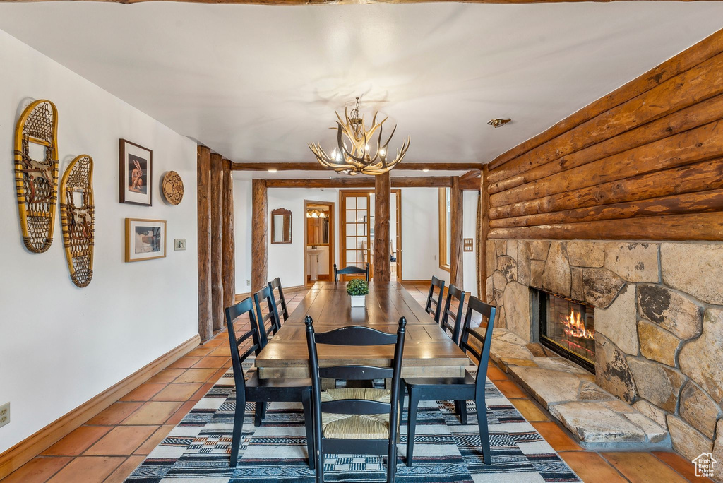 Dining room with rustic walls, a chandelier, a fireplace, tile patterned floors, and baseboards