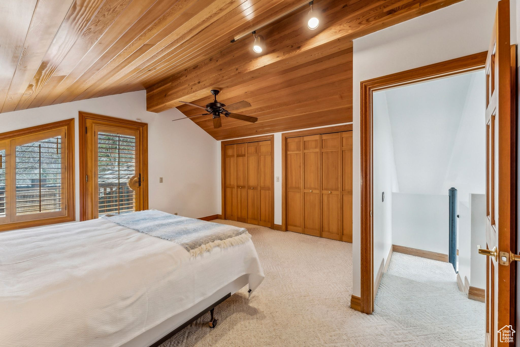 Bedroom with light colored carpet, multiple closets, vaulted ceiling with beams, and baseboards