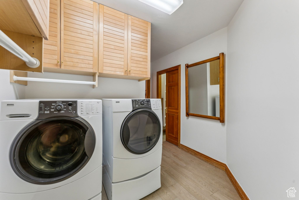 Clothes washing area featuring cabinet space, washing machine and clothes dryer, light wood finished floors, and baseboards