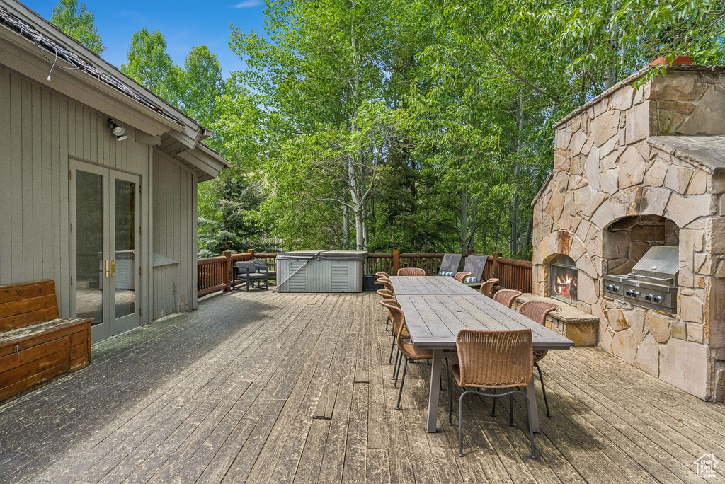Deck featuring french doors, an outdoor stone fireplace, grilling area, outdoor dining area, and view of scattered trees