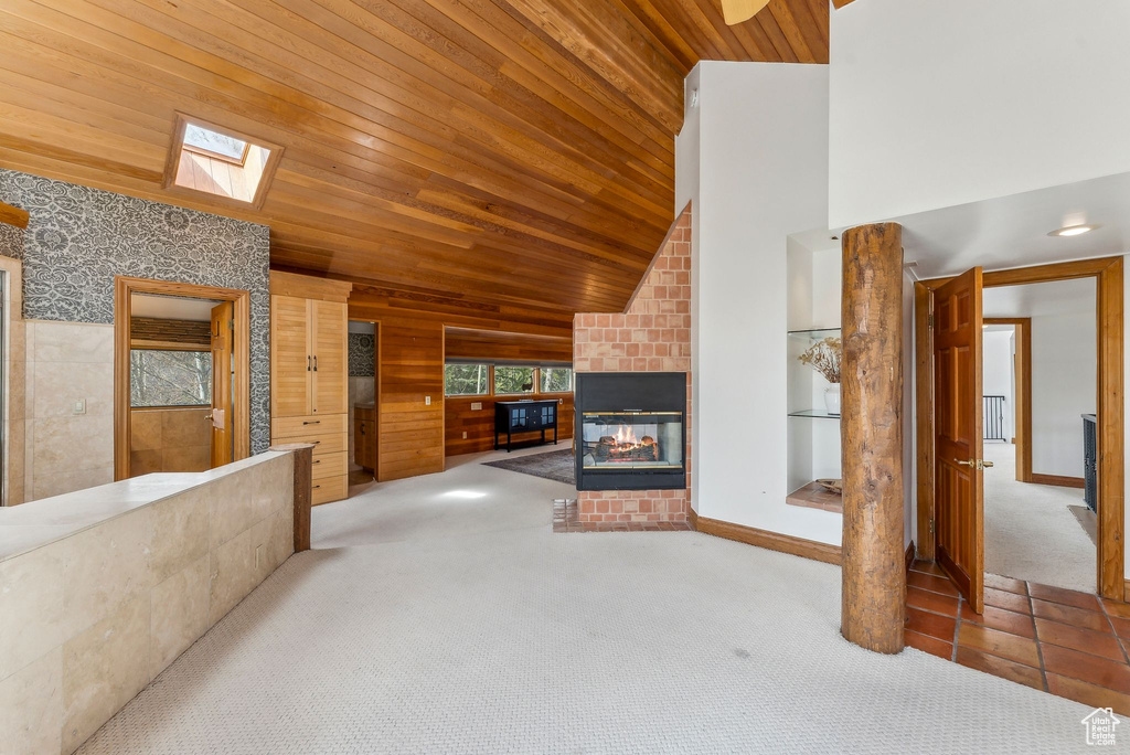 Unfurnished living room featuring wood ceiling, carpet flooring, a tiled fireplace, high vaulted ceiling, and a skylight