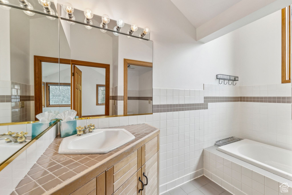 Full bathroom with tile patterned floors, vaulted ceiling, tile walls, a bath, and vanity