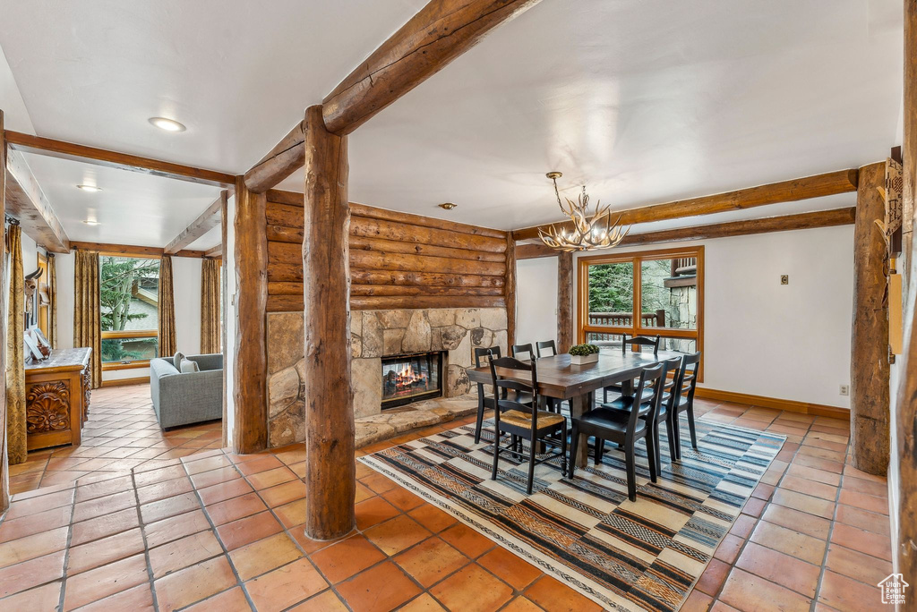 Dining space featuring beamed ceiling, log walls, a chandelier, baseboards, and a stone fireplace