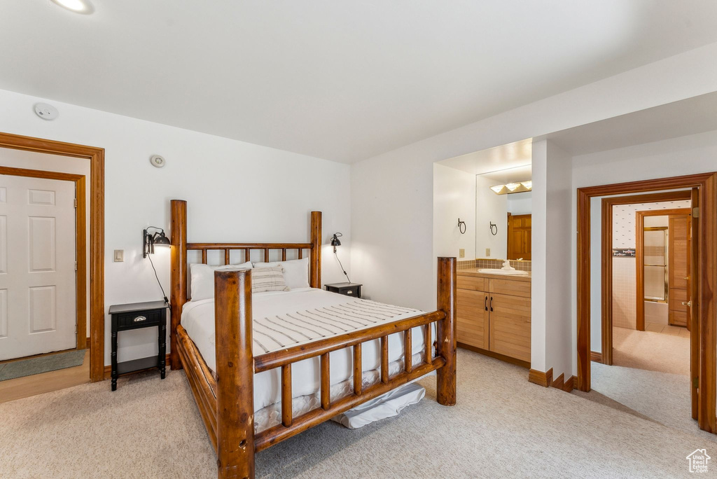 Bedroom featuring baseboards, ensuite bathroom, light colored carpet, and a sink