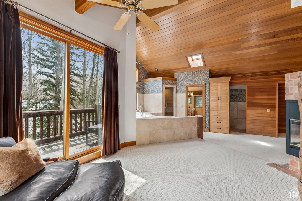 Living room featuring wooden ceiling, vaulted ceiling with skylight, a ceiling fan, carpet, and baseboards