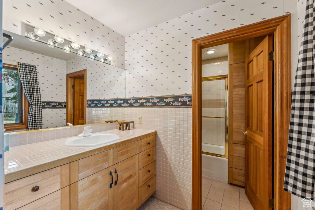 Bathroom featuring tile patterned floors, wallpapered walls, shower / bath combination with glass door, and vanity