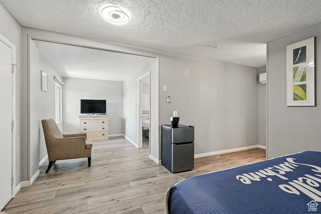 Bedroom with light wood finished floors, baseboards, freestanding refrigerator, and a textured ceiling
