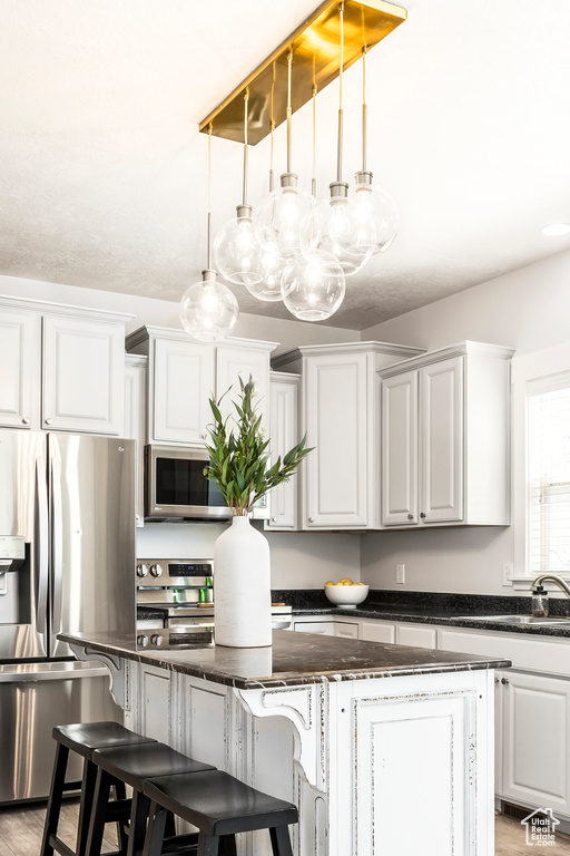 Kitchen featuring a kitchen island, a breakfast bar area, a sink, appliances with stainless steel finishes, and decorative light fixtures