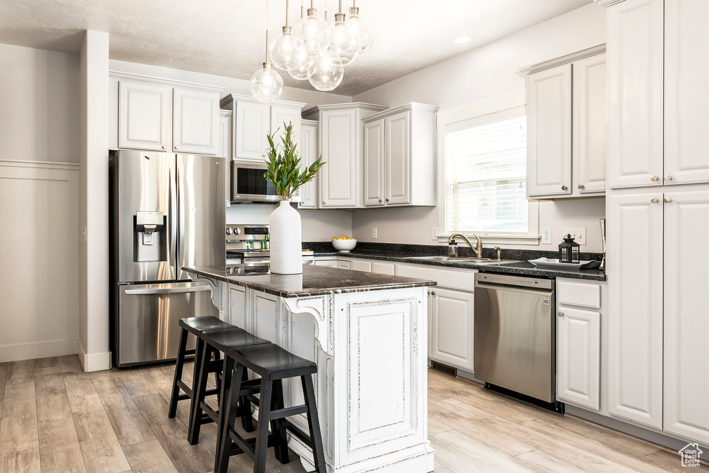 Kitchen featuring appliances with stainless steel finishes, a sink, light wood-style flooring, a center island, and pendant lighting