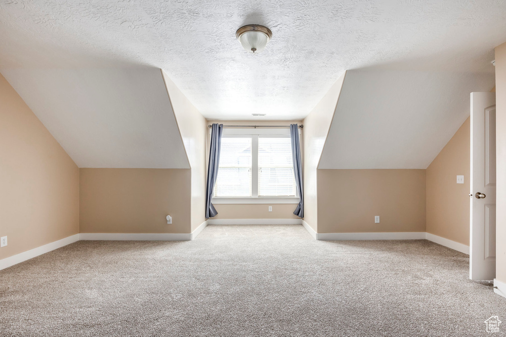 Bonus room featuring carpet flooring, vaulted ceiling, a textured ceiling, and baseboards