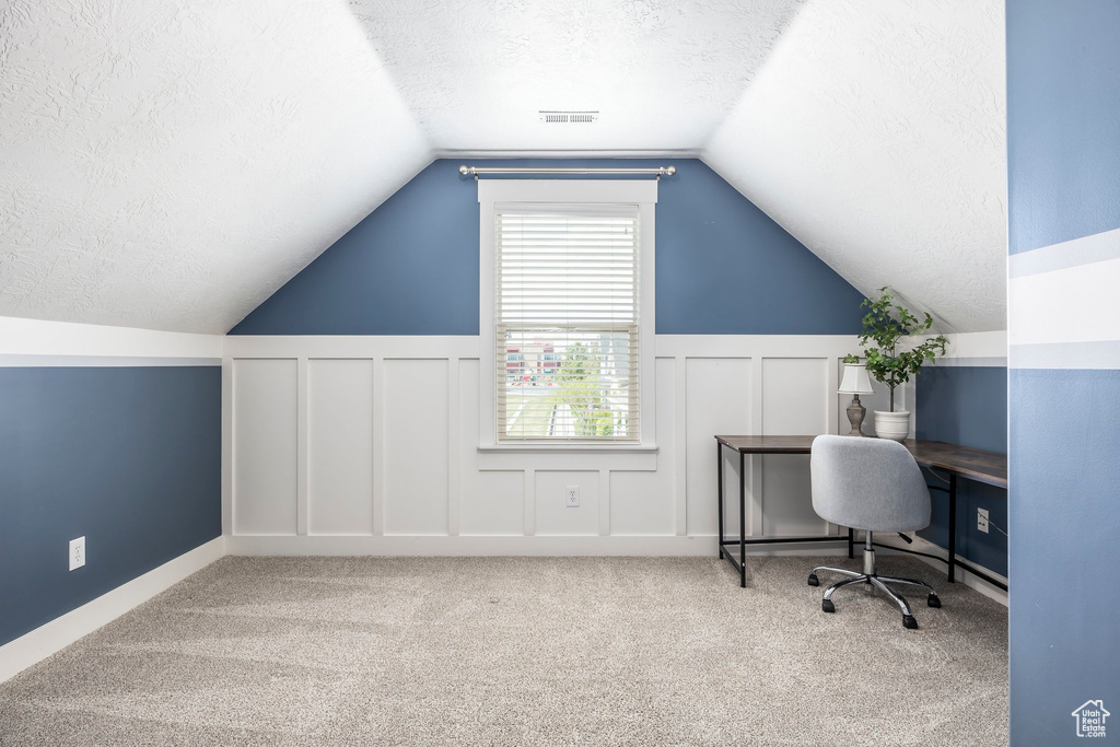 Carpeted home office with visible vents, a decorative wall, a textured ceiling, and lofted ceiling