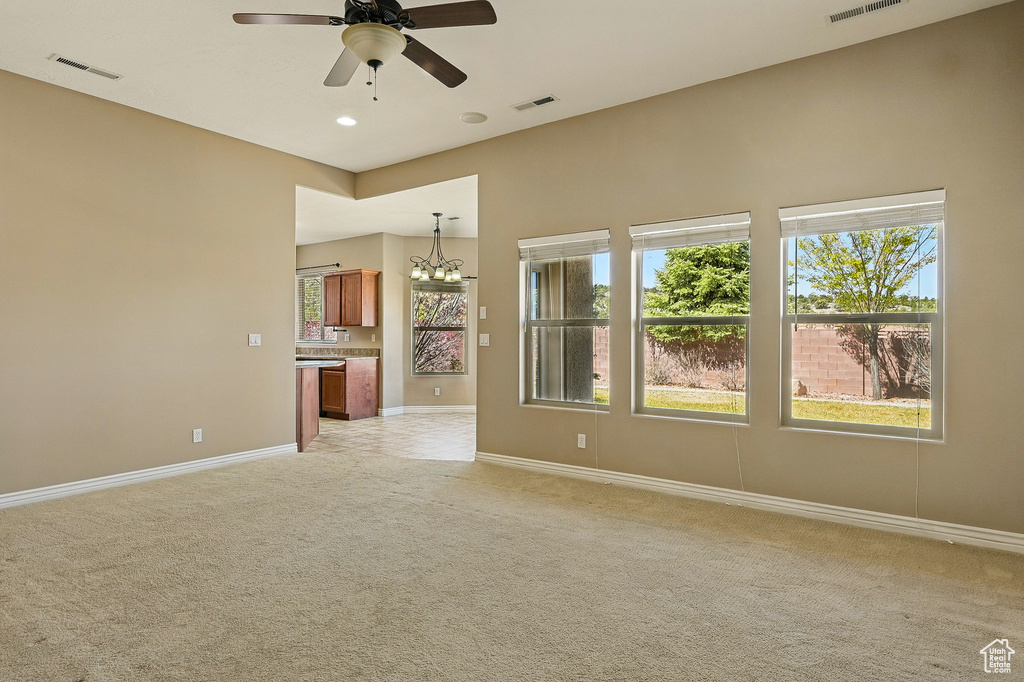 Unfurnished living room with baseboards, light colored carpet, visible vents, and ceiling fan with notable chandelier